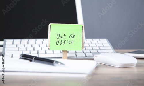 Out of office message on sticky note with computer. photo