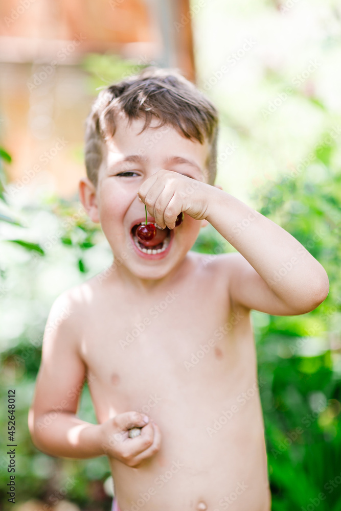 Fototapeta premium Little boy holds cherries in his mouth