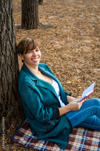 middle-aged woman reads a book, takes notes in a notebook, autumn park. orange leaves. concepts about senior people