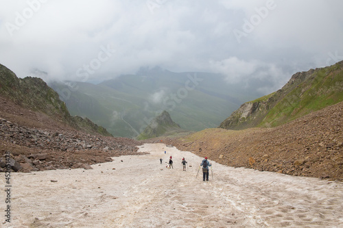 A group of people goes down the glacier. Mountain valley in the background.