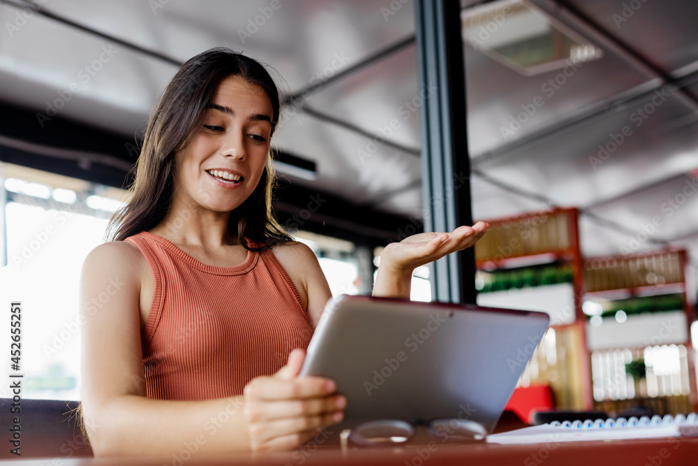 A cute girl is emotionally talking on a video call on a digital tablet, sitting at a table in a cafe A cute girl is emotionally talking on a video call on a digital tablet, sitting at a table in a cafe