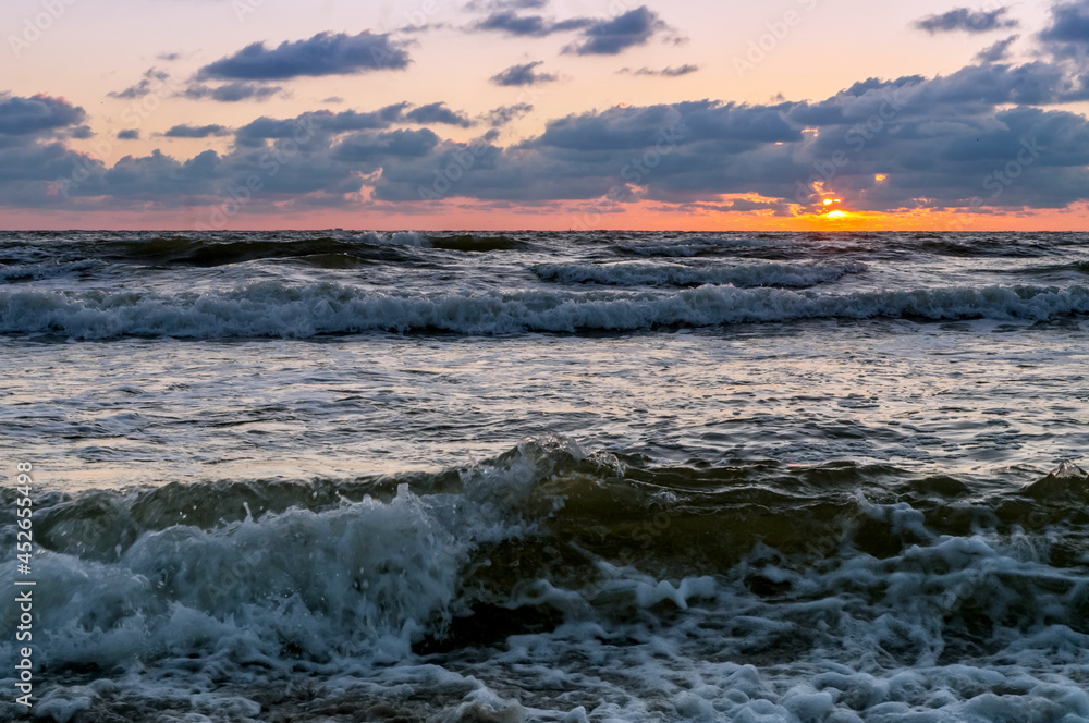 Fototapeta premium Sunset over the sea. Reflection of sunlight in the sea waves. Red and yellow sky in the rays of the sunset.