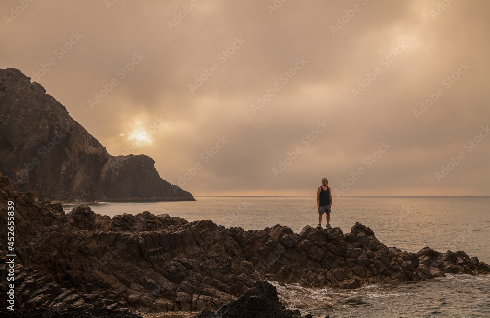 Fototapeta premium Man standing on rock looking at view of scenic beach during sunrise