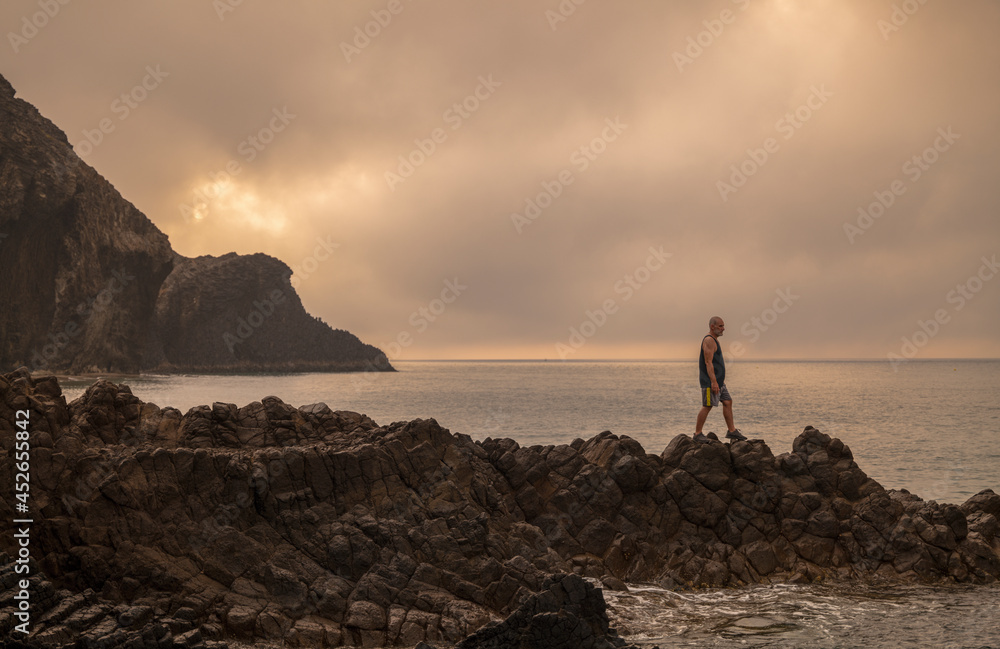 Man standing on rock looking at view of scenic beach during sunrise
