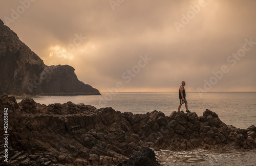 Man standing on rock looking at view of scenic beach during sunrise