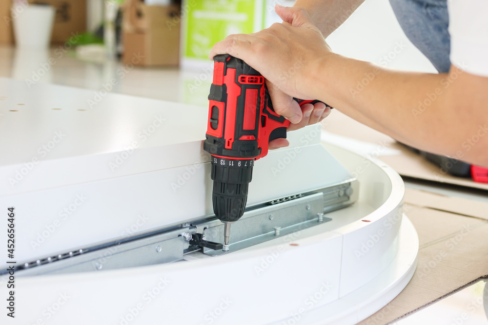 man assembling white table furniture at home using cordless screwdriver man assembling white table furniture at home using cordless screwdriver