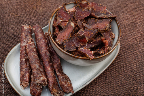 traditional South African Cured meat snacks, Biltong and dry wors, in grey bowl on rustic brown fabric with copy space photo