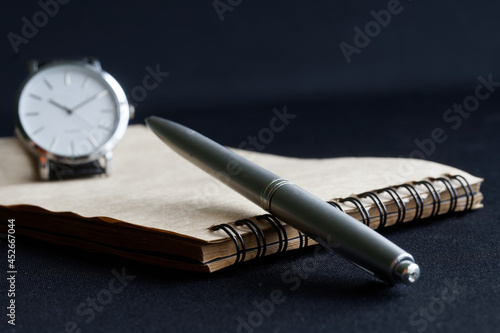 Metalized ballpoint pen and a spring-loaded notebook lie next to the wristwatch. Concept of will, notary, memoir and deadline. Selective focusing