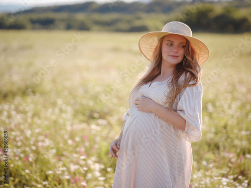 Beautiful pregnant woman in dress and hat relaxing outside in chamomile field. Right choice for your baby digital detox and reconnecting with nature.