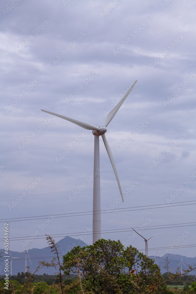 Windmill - Wind turbine below the mountain on the agriculture land. Alternate energy source generator with environment friendly. Wind turbines for ecological power supply 