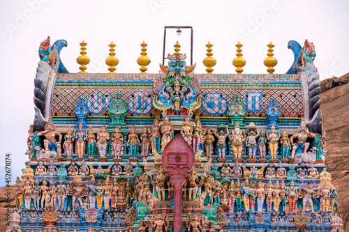 Old south indian temple in close up with full architecture details. Multi colour temple tower in south India surrounded by mountains and rocks.. photo
