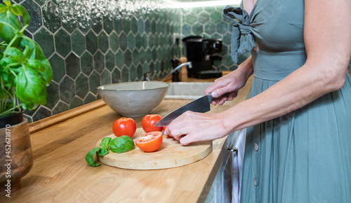 fwoman cutting fresh tomatoes and basil in modern kitchen interior with white furniture home background photo