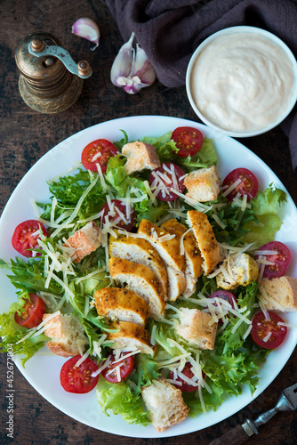 Caesar salad with chicken breast, croutons and parmesan sauce on a wooden table