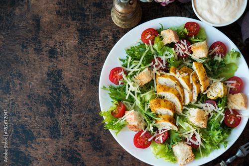 Fotografie Caesar salad with chicken breast, croutons and parmesan sauce on a wooden table,