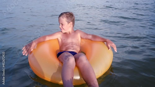 A cute boy 6-7 years old in an inflatable orange circle sways on the sea waves. Happy childhood, travel and leisure