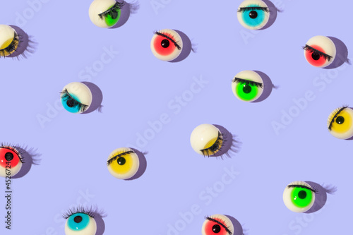 Creative pattern made with eyeball figurines with eyelashes on pastel purple background. Halloween minimal creative concept. Rainbow colored eyes. Modern fashion aesthetic or cosmetic idea.