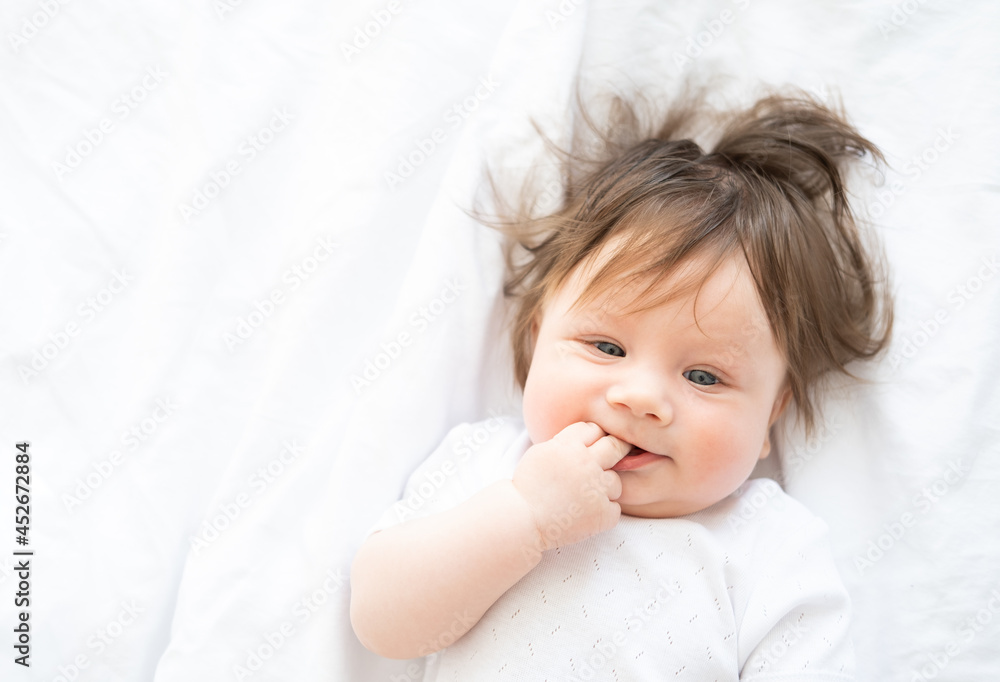 portrait of funny baby girl with finger in a mouth smiling and lying on a white bedding at home. portrait of funny baby girl with finger in a mouth smiling and lying on a white bedding at home.