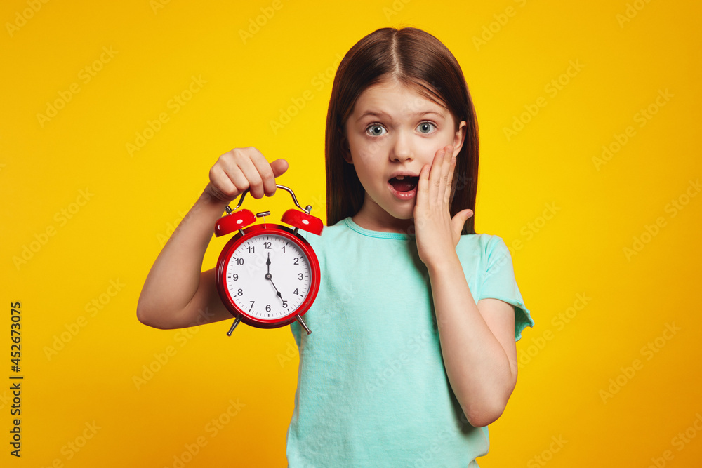 Young little girl kid holding classic bell alarm clock over isolated yellow background, shocked for mistake, expression of fear, scared in silence Young little girl kid holding classic bell alarm clock over isolated yellow background, shocked for mistake, expression of fear, scared in silence