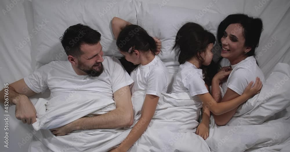 Top view of Caucasian family with two children laughing and talking in bed with white sheets. High angle shooting. A family of four is sleeping. Mom, dad and daughters good night, restful sleep 4k Stock Video | Adobe Stock