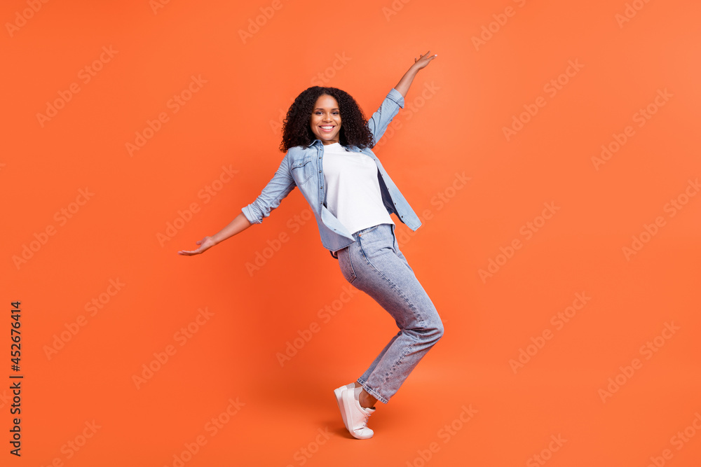Full length photo of funky millennial brunette lady dance wear jeans shirt shoes isolated on orange background Full length photo of funky millennial brunette lady dance wear jeans shirt shoes isolated on orange background