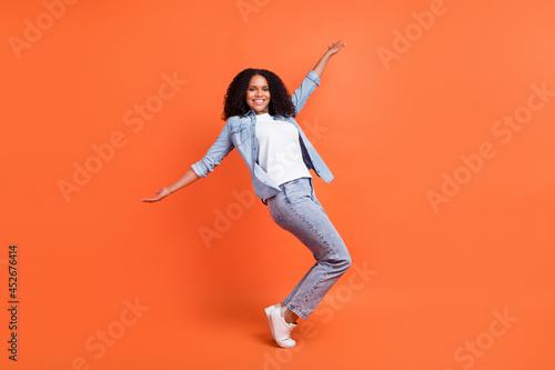 Full length photo of funky millennial brunette lady dance wear jeans shirt shoes isolated on orange background