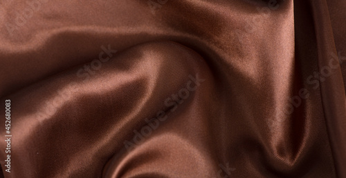 brown or chocolate silk satin fabric texture background.Cloth soft wave. Creases of satin