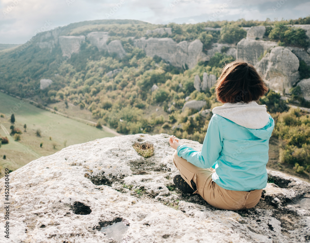 The traveler sits on the edge of a cliff. Young woman resting and enjoying the beauty of nature from above.