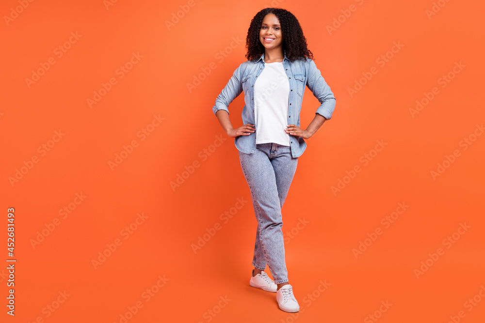 Full length photo of cute millennial brunette lady go wear jeans shirt shoes isolated on orange background Full length photo of cute millennial brunette lady go wear jeans shirt shoes isolated on orange background