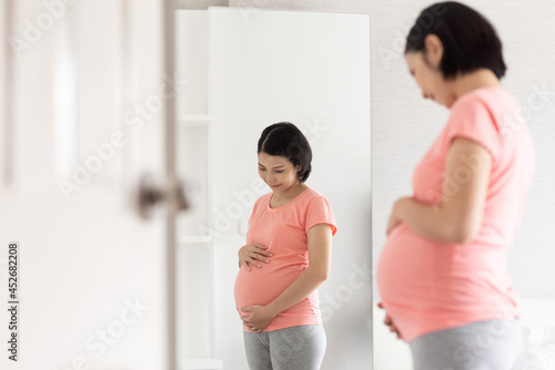 Asian pregnant woman standing touching belly. © eggeeggjiew