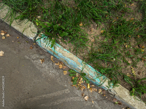 Damadged old curb painted aquamarine needs to be replaced. Yellow leaves on asphalt. Top view photo