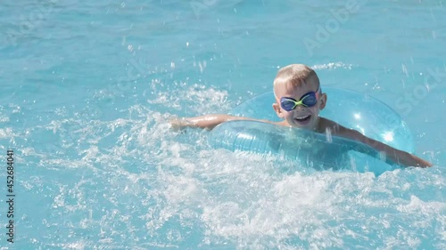 Little boy in swimming pool, child having fun, sitting on blue swimming ring, playing under water. Summer travel family hotel vacation tourists photo