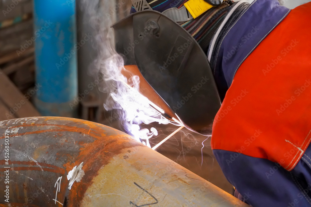 Manual arc welding. A welder makes a weld on a pipeline for oil