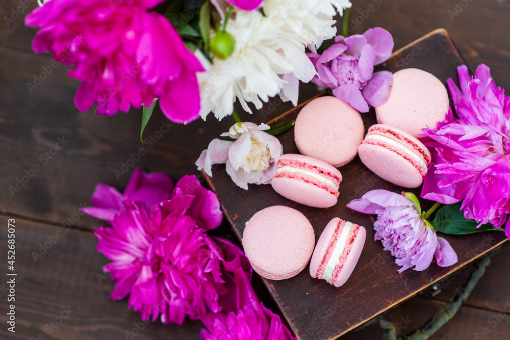 Pink macaroons lie on a wooden box surrounded by peony flowers Pink macaroons lie on a wooden box surrounded by peony flowers