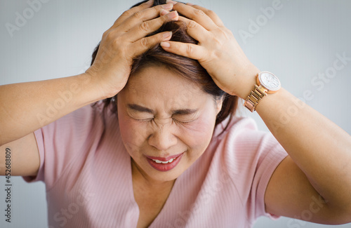 Middle age senior Asian woman feeling pain from sudden headache and brain stroke attack and hold her head with a distorted and writhe face. Concept of brain and head problem