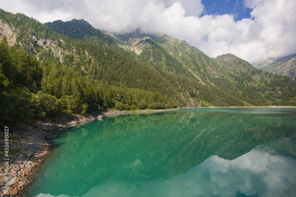 Enchanted view of the Lago dei Cavalli, Alpe Cheggio. The clear water, the rich vegetation, the blue sky and the white clouds during summer season, Piedmont, Italy