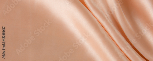 Rose Gold silk satin fabric texture background.Cloth soft wave. Creases of satin