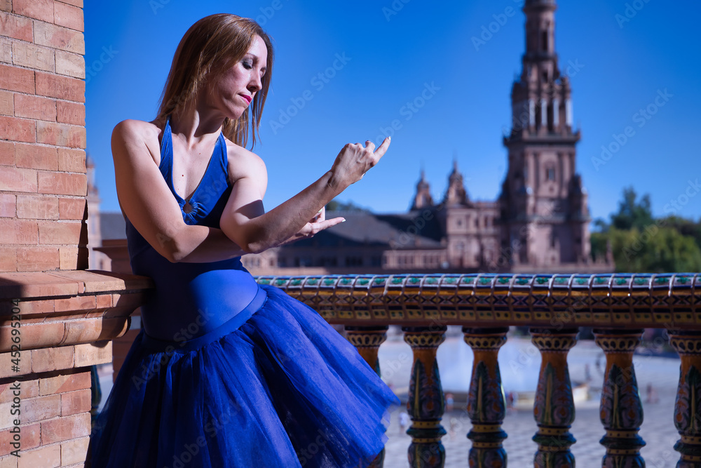 Obraz premium Hispanic adult female classical ballet dancer in blue tutu doing figures on the terrace of a plaza next to a beautiful tiled balustrade.