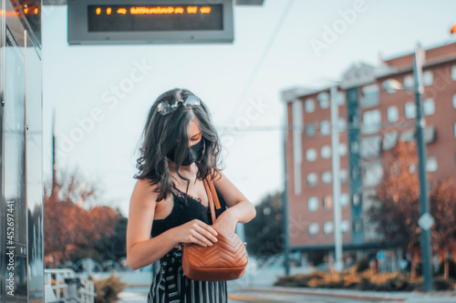 Mujer mayor morena con mascarilla revisando su bolso en la estación de tren junto a la ciudad