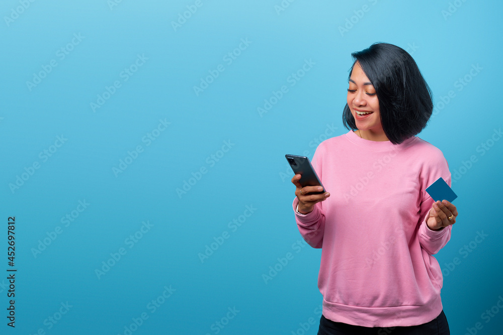 Beautiful smiling asian woman using mobile phone and holding credit card on blue background Beautiful smiling asian woman using mobile phone and holding credit card on blue background