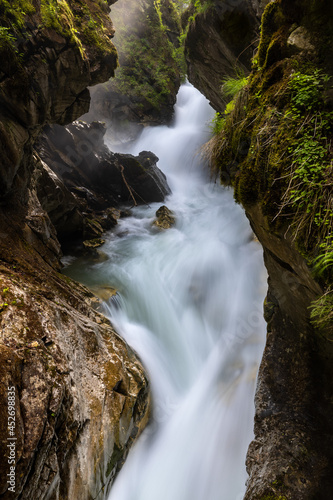 Fototapeta Naklejka Na Ścianę i Meble -  Close up of a mountain creek rushing into a gorge, surrounded by rocks and vegetation