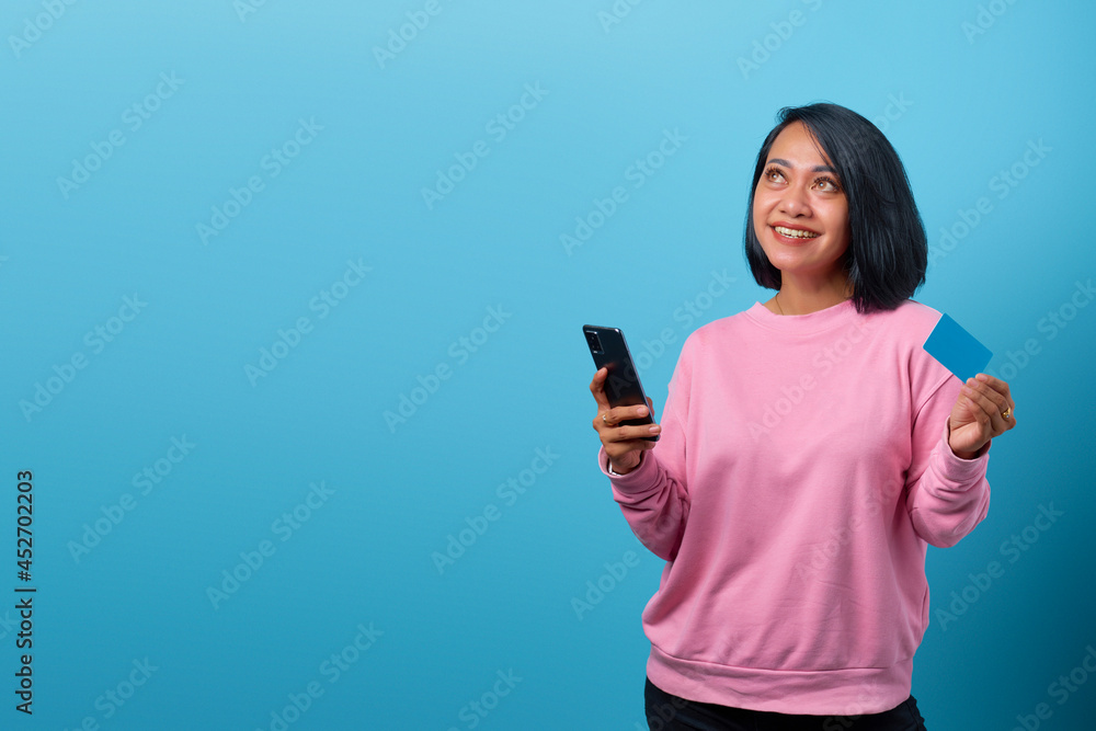 Portrait of beautiful smiling asian woman using mobile phone and holding credit card and looking up empty space Portrait of beautiful smiling asian woman using mobile phone and holding credit card and looking up empty space