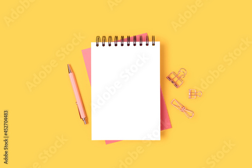 Workspace with open notepad mockup and pink stationery on a yellow background. Business layout.