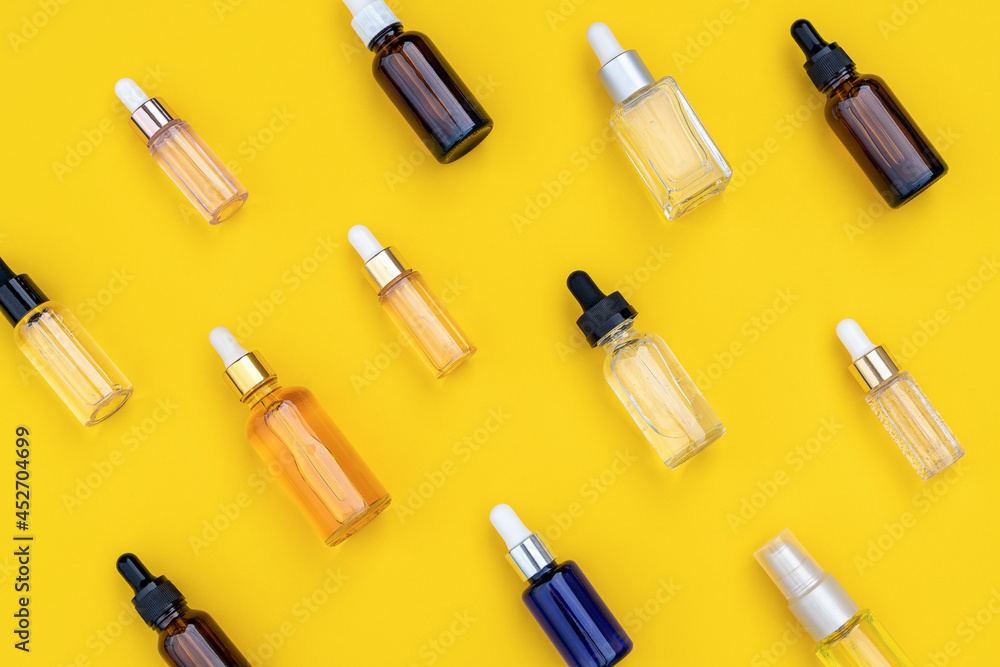 Abstract pattern of serums in glass bottles with dropper on bright yellow background. Creative layout, cosmetic pattern, flat lay. For packaging design, printing on fabric, paper