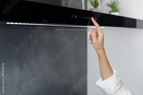 Female adjusting cooker hood while cooking in kitchen
