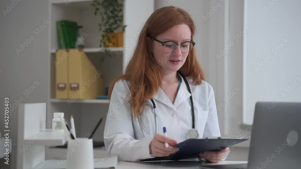 Doctor telemedicine service for clients. Spbas Skilled female therapist with loose red hair talks to patient looking into history at videochat in clinic office Doctor telemedicine service for clients. Spbas Skilled female therapist with loose red hair talks to patient looking into history at videochat in clinic office