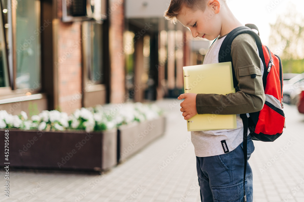 Back to school. Cute child with backpack holding notepad and training books going to school. Boy pupil with bag. Elementary school student going to classes. Kid walking outdoor on the city street.