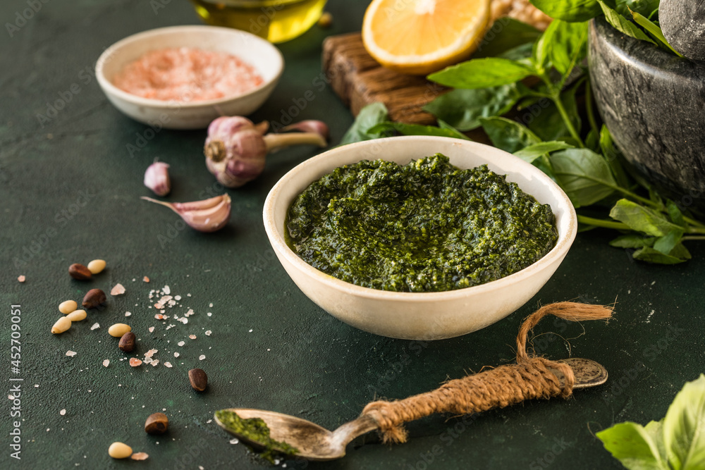 Pesto sauce in bowl with ingredients on rustic green table. Traditional Italian pesto recipe for making fettuccine, pasta, bruschetta. Pesto sauce in bowl with ingredients on rustic green table. Traditional Italian pesto recipe for making fettuccine, pasta, bruschetta.