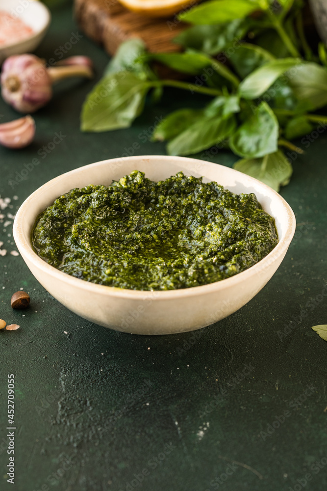  Pesto sauce in bowl with ingredients on rustic green table. Traditional Italian pesto recipe for making fettuccine, pasta, bruschetta.