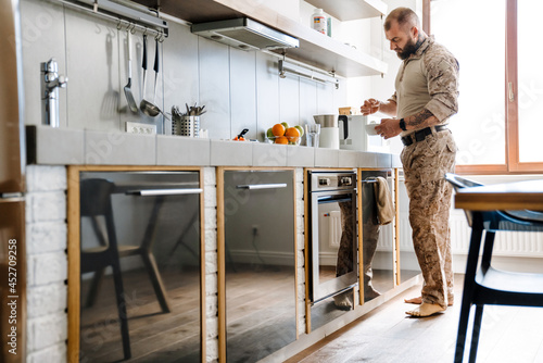 White military man wearing uniform drinking tea in kitchen at home