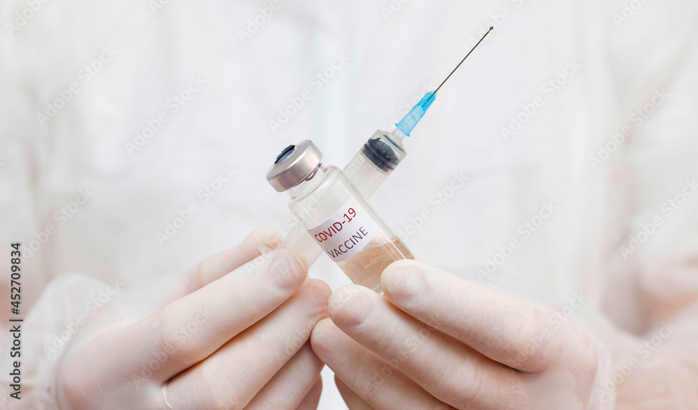 A man in a medical uniform holds an ampoule with a coronavirus vaccine in front of him. A man in a medical uniform holds an ampoule with a coronavirus vaccine in front of him.